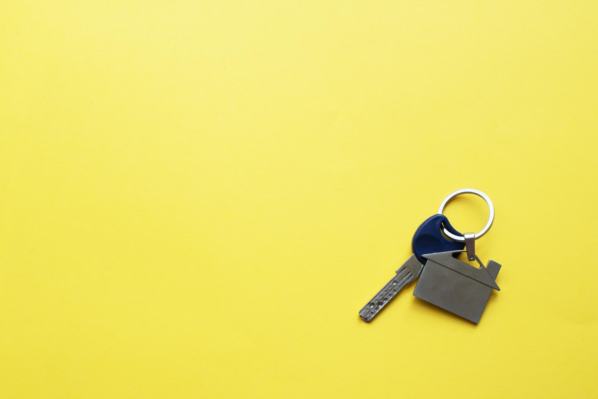 Key with a keychain in the form of a house on a bright yellow background. Place for inscriptions.